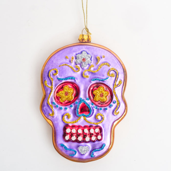 a purple sugar skull ornament with a gold border, yellow floral eyes, a red nose, & gold, blue, & silver glitter accents