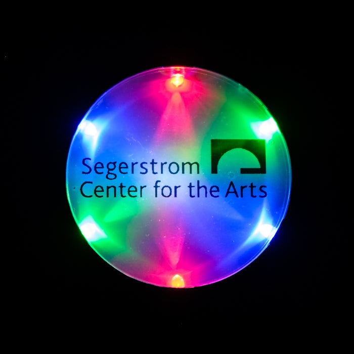 An upclose view of a lit LED circular pendant necklace with multicolored lights & the Segerstrom Center for the Arts logo