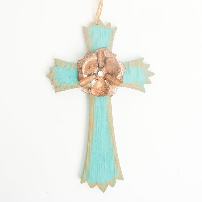A wooden cross ornament in a faded light blue color with a bronze flower & a silver gemstone in the center