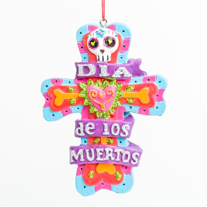 a pink blue & red cross ornament w/ orange bones & a pink heart, w/ a white skull & glittery purple Día de los Muertos banner