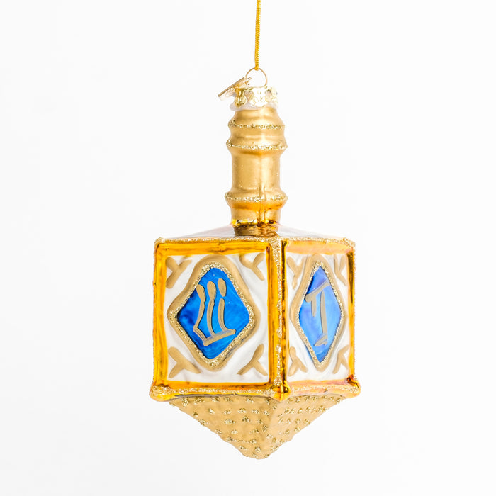 a 3-quarter view of a gold dreidel ornament with blue and gold Hanukkah symbols on it, displayed under a bright light
