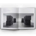 inside the "Forged Steel" book showing a 2-page black & white image of 8 steel cubes in stacks of 2 inside an empty room