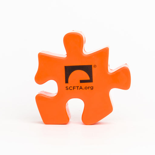 An Orange Puzzle Piece Shaped Stress Ball with the Segerstrom Center for the Arts logo and SCFTA.org on it in Black.