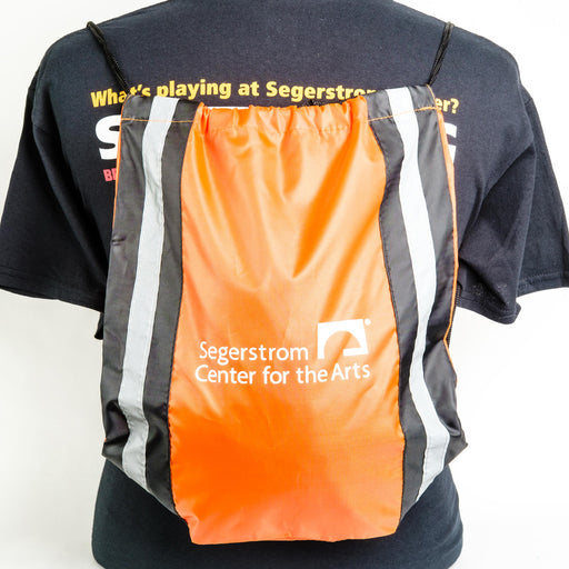 An Orange Drawstring Bag with vertical Black & Silver Reflective Stripes & the Segerstrom Center for the Arts logo in white