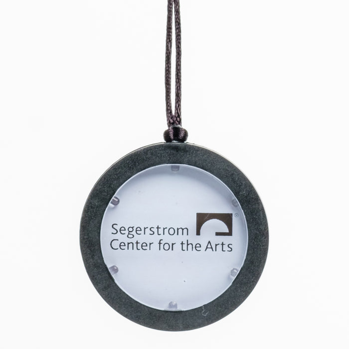 An upclose view of a LED circular gray pendant necklace with a white center & the Segerstrom Center for the Arts logo in Black 